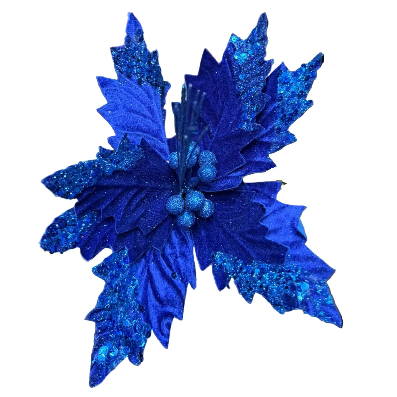 A close-up of a glittery royal blue artificial poinsettia flower with textured leaves and small berry-like accents, held in a hand. The background shows a cluttered workshop or studio environment with cardboard boxes, cables, and other decor items.
