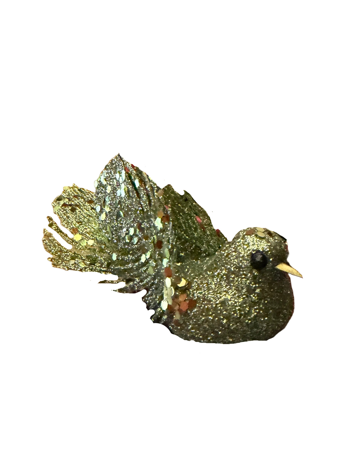A hand holds a green glitter bird Christmas ornament with a metallic gold tail, in front of a red shopping basket filled with holiday decorations on a wooden floor.
