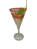 A clear martini-style glass filled with a layered drink, garnished with a pink sugar-rimmed edge, green leaves, and orange slices, photographed on a plain light background.